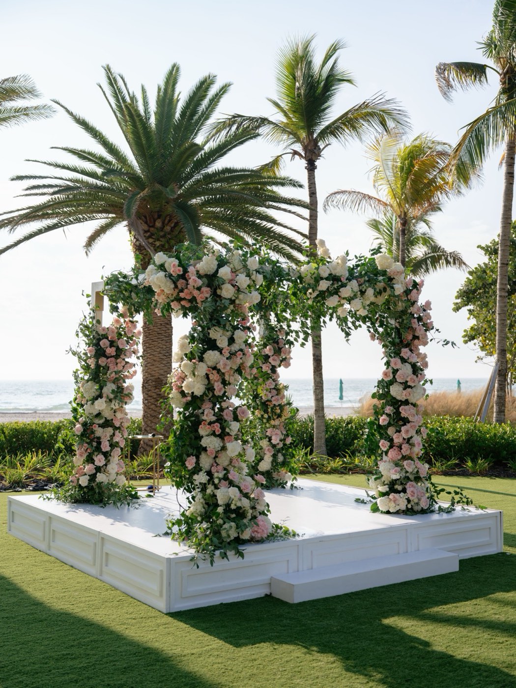 Coastal ceremony stage with lush floral columns and palm trees