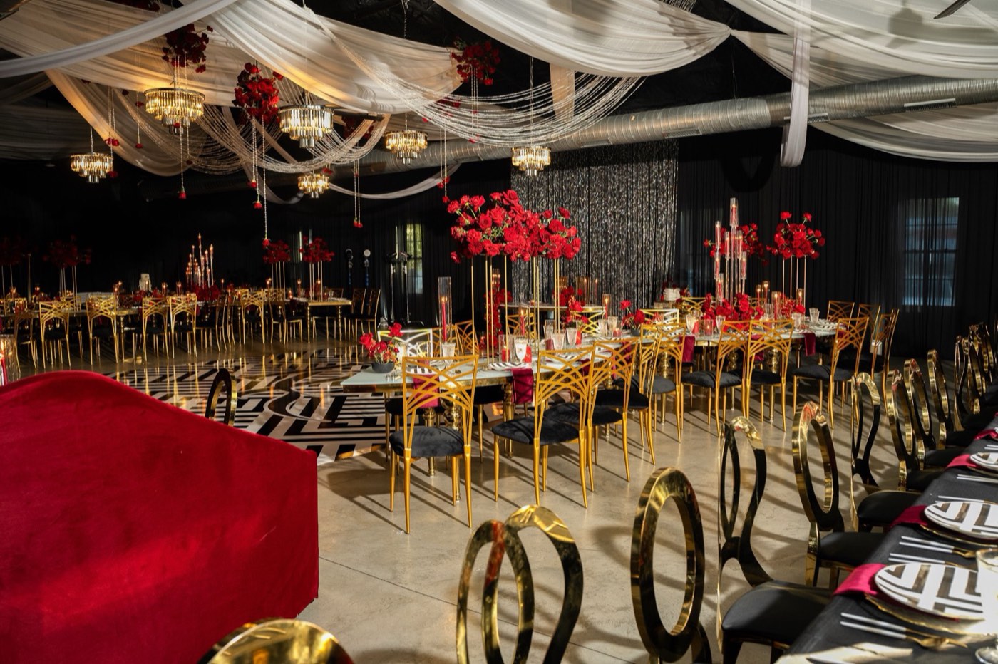 Black and red reception with gold chairs, chandeliers, and ceiling draping