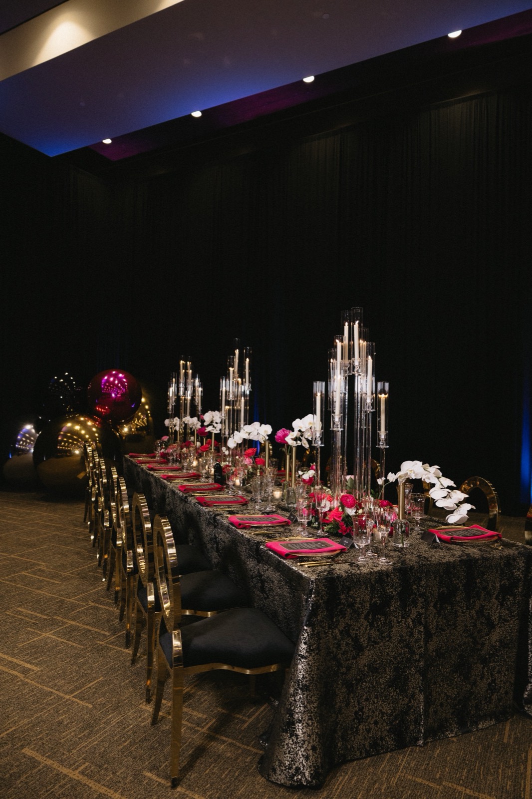 Black tablescape with tall candle holders, pink florals, and gold chairs