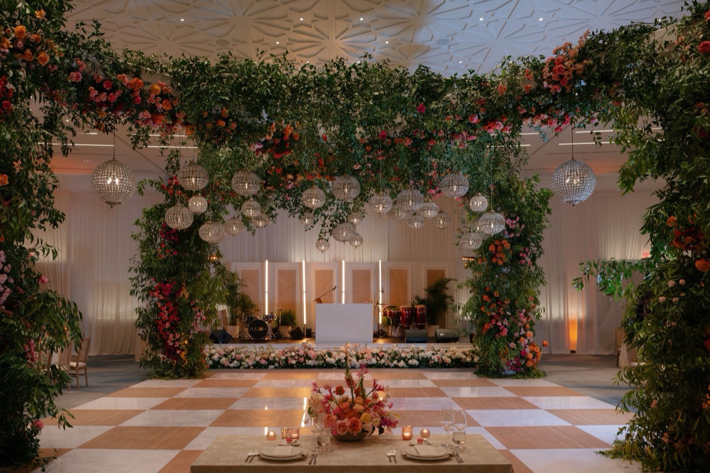 Reception dance floor framed by lush floral canopy and hanging chandeliers