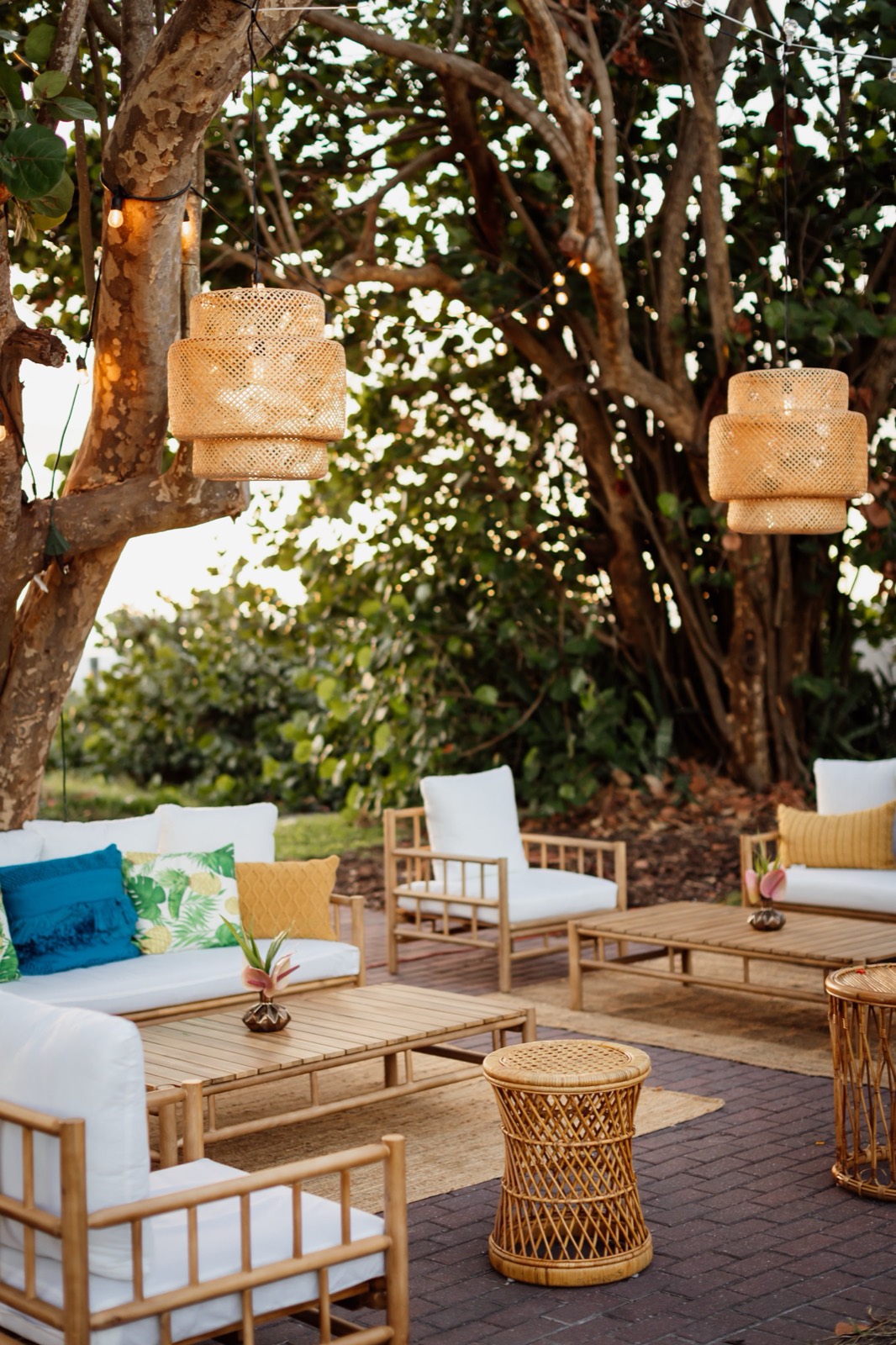 Outdoor lounge setting with rattan furniture, woven pendants, and tropical pillows