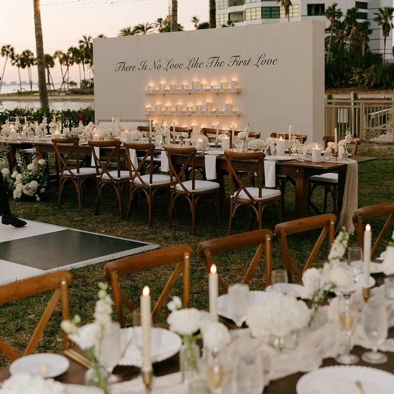 Elegant outdoor reception with a candle wall, white orchids, and wood chairs