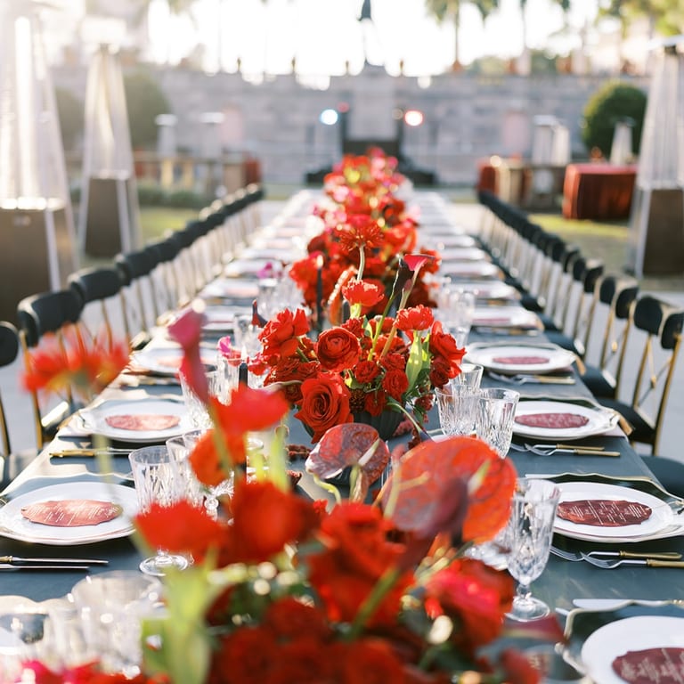 Long outdoor reception table with bright red floral centerpieces