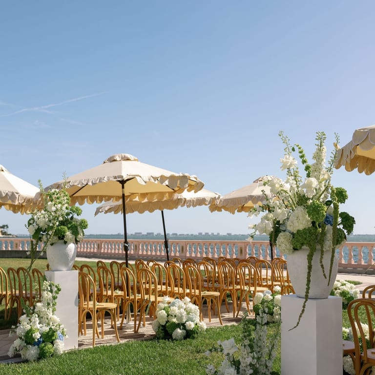 Waterfront wedding ceremony with parasols, white florals, and gold chairs