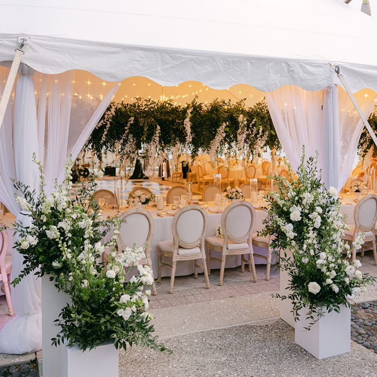 White-draped outdoor reception with greenery, florals, and soft lighting