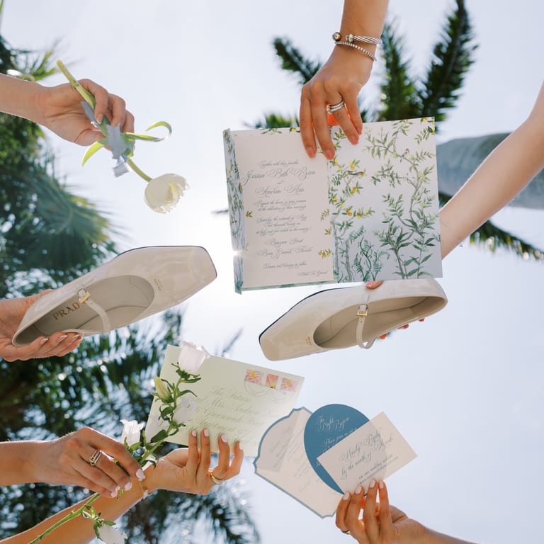 Wedding stationery and place-setting details arranged beneath palm trees